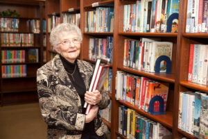 Woman standing in front of library shelf holding book.