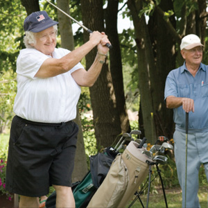 Senior man and woman playing golf outdoors.